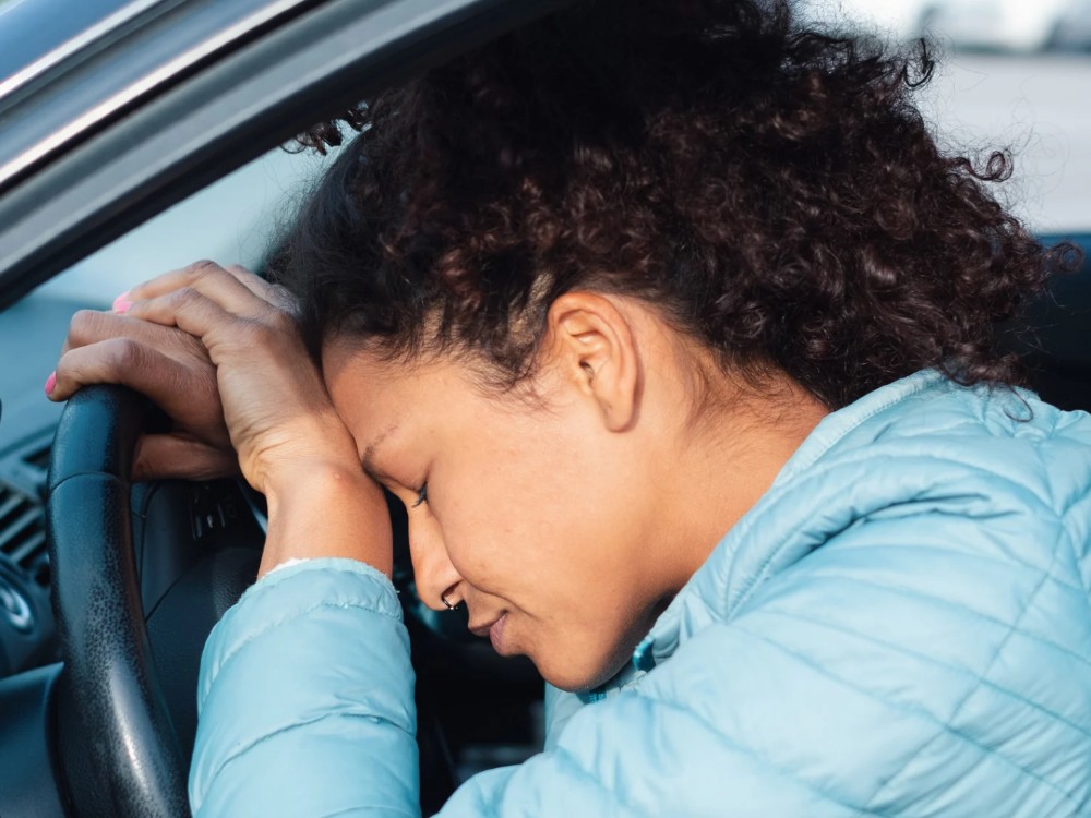 Exhausted woman with her head against a car steering wheel.