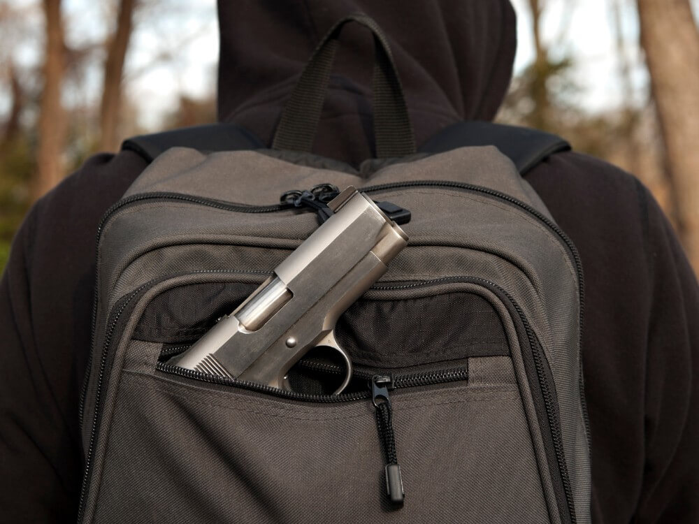 Gun sticking out of a dark gray backpack.