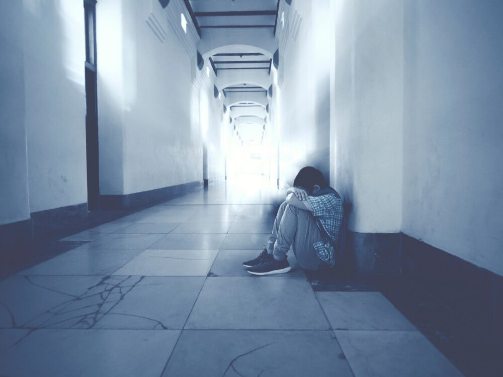Boy with head in lap in an empty hallway.