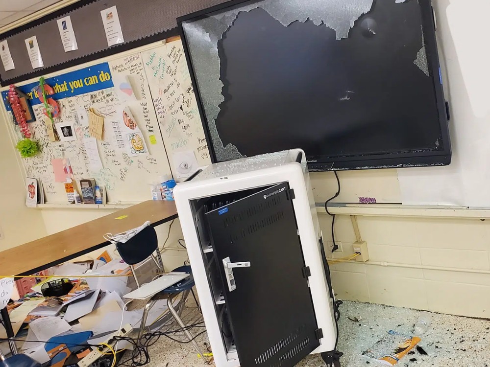 School classroom destroyed with a broken smart screen, glass everywhere, and graffiti on the walls.