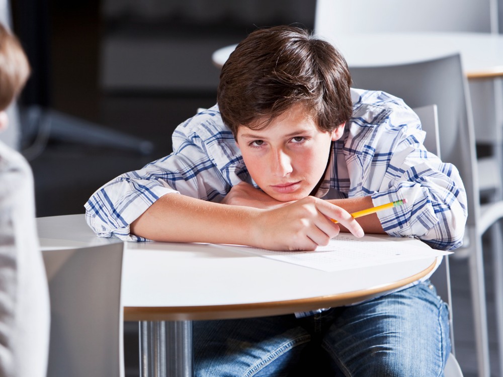 Student sitting at a desk with his head on his arms.