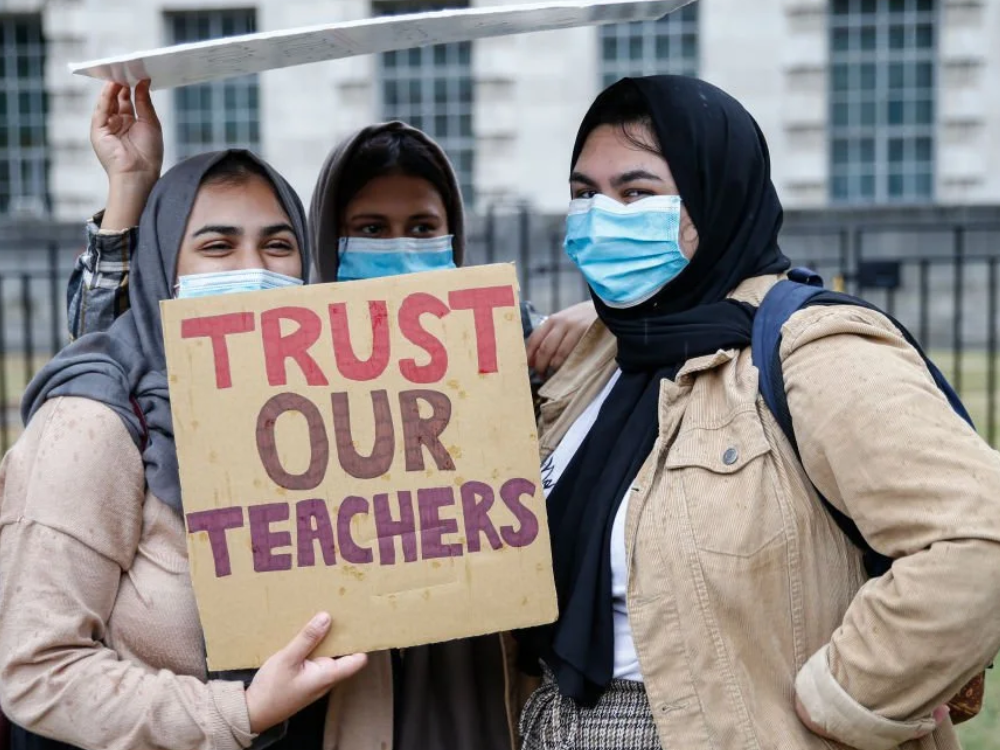 Women holding a sign that says - Trust our teachers.